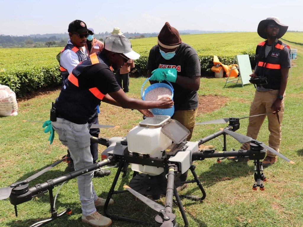 A team of young African agritech professionals preparing a large agricultural drone for crop spraying and monitoring in a lush green field.