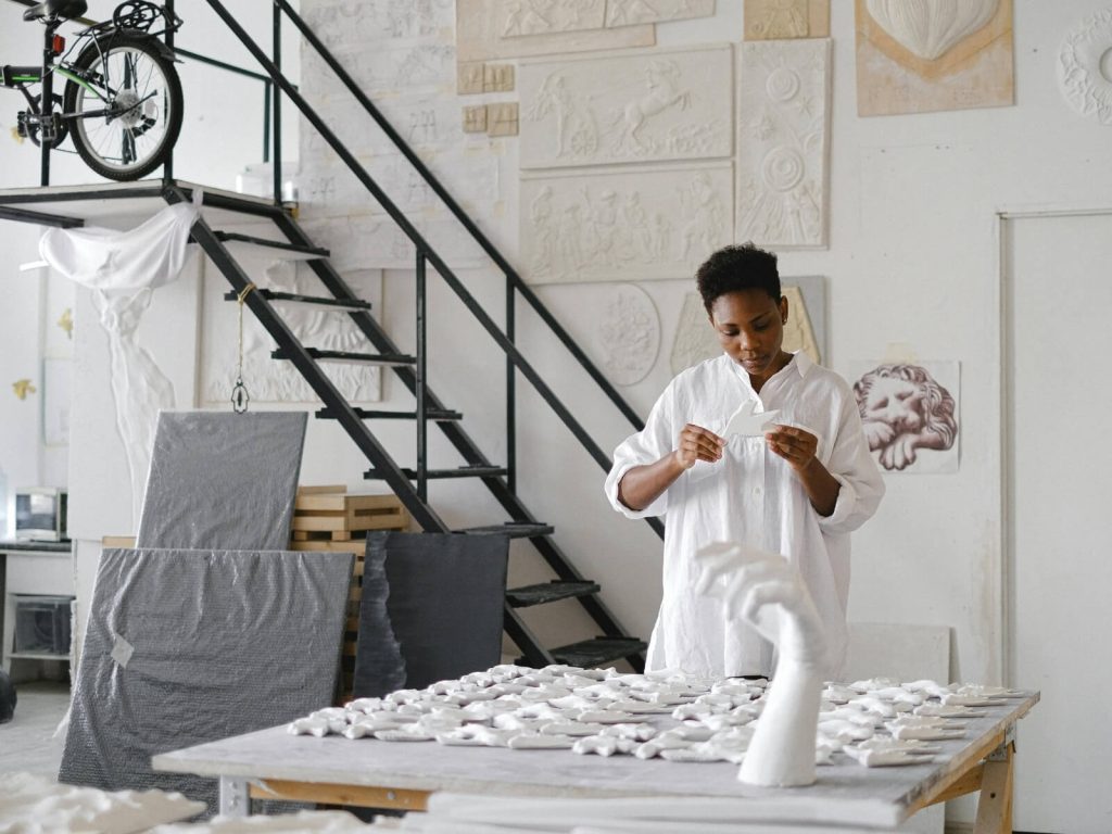 A young African woman sculptor in a white studio working on plaster art pieces, symbolizing the growth of the creative sector for women and youth in Africa.