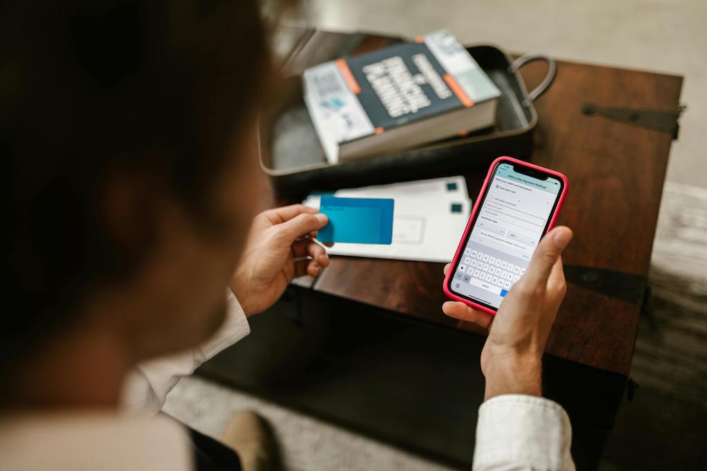 A young entrepreneur using a smartphone and a payment card for digital transactions, with a financial planning book in the background