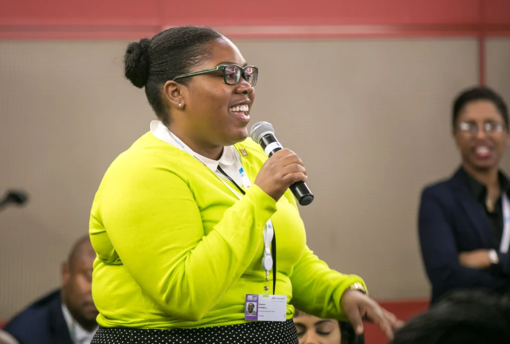 A Black professional woman speaks confidently at a business conference in South Africa, illustrating the principle of participation central to Black Economic Empowerment (BEE).