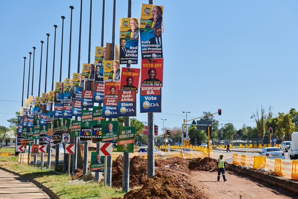 A row of South African election posters, including the EFF's, illustrating the competitive political climate as the Malema verdict timing is questioned.