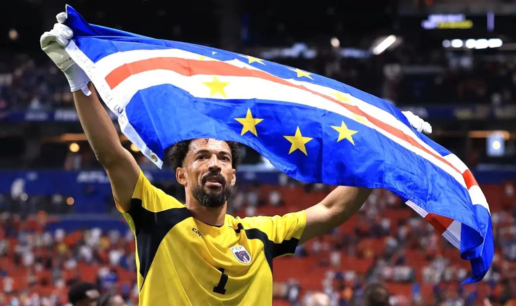 Cabo Verde goalkeeper holding up the national flag in a packed stadium, symbolizing the success of African football diaspora players.