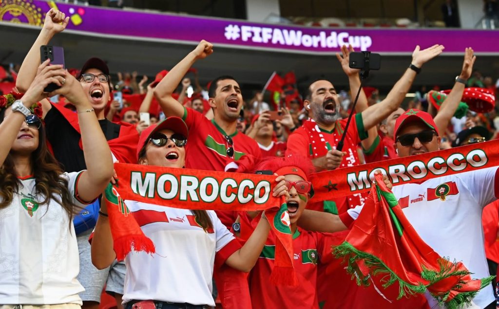 Moroccan football fans celebrating in a World Cup stadium with team scarves, showcasing the global community behind African football diaspora players.